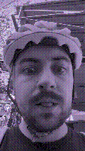 a selfie of a white person, wearing either headphones or a helmet, making an odd expression. the photo is edited to be colorized into a monochrome purple-ish color palette.
